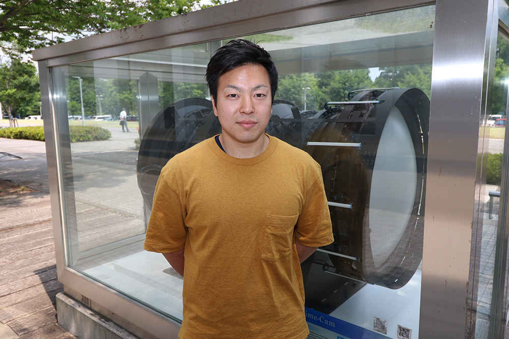 東京大学宇宙線研究所の林航平・学振特別研究員、柏キャンパス内のHSC模型前で撮影